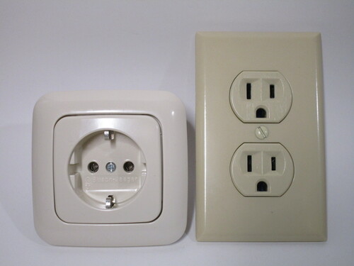 Front view of a Schuko socket, on the left, and a standard American duplex one on the right. Both are coloured beige. The American socket is taller than the Schuko one, though the width is roughly the same.