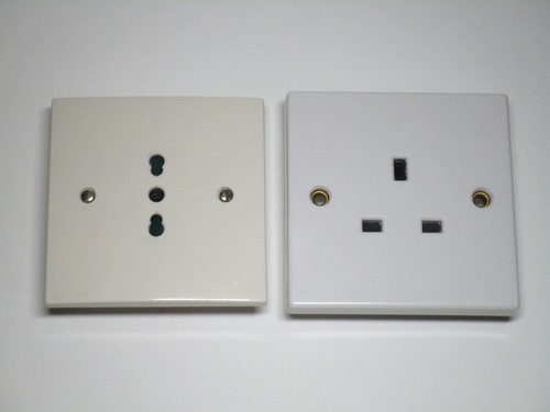 Comparison view of an Italian Bipasso socket from the Vimar Mascot series, on the left, and a one-gang UK socket on the right. Both are single-block devices, with mounting screws at the front.