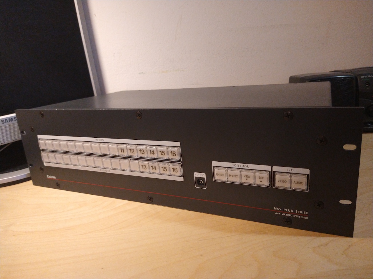 A front view of the Extron matrix switcher. There are 16 input and 16 output buttons, alongside 4 control buttons.